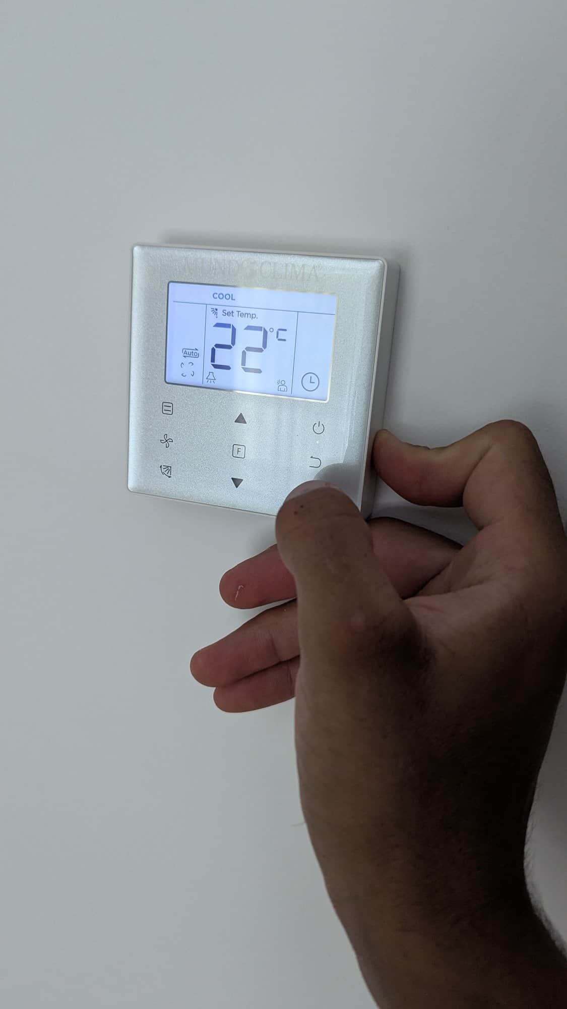Hand die de temperatuur instelt op een airco-wandbediening.