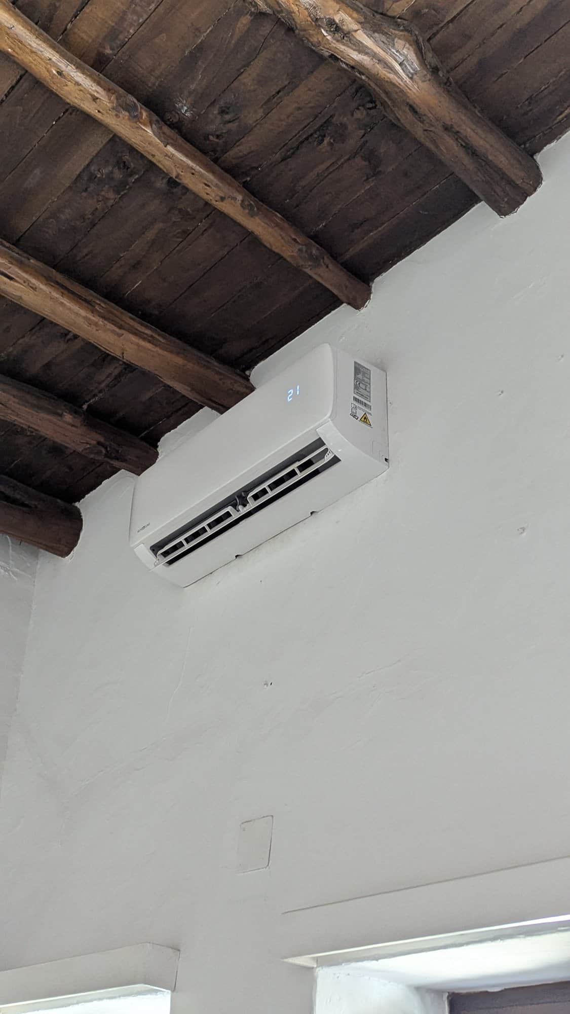 Wandunit van de airco onder een houten balkenplafond.