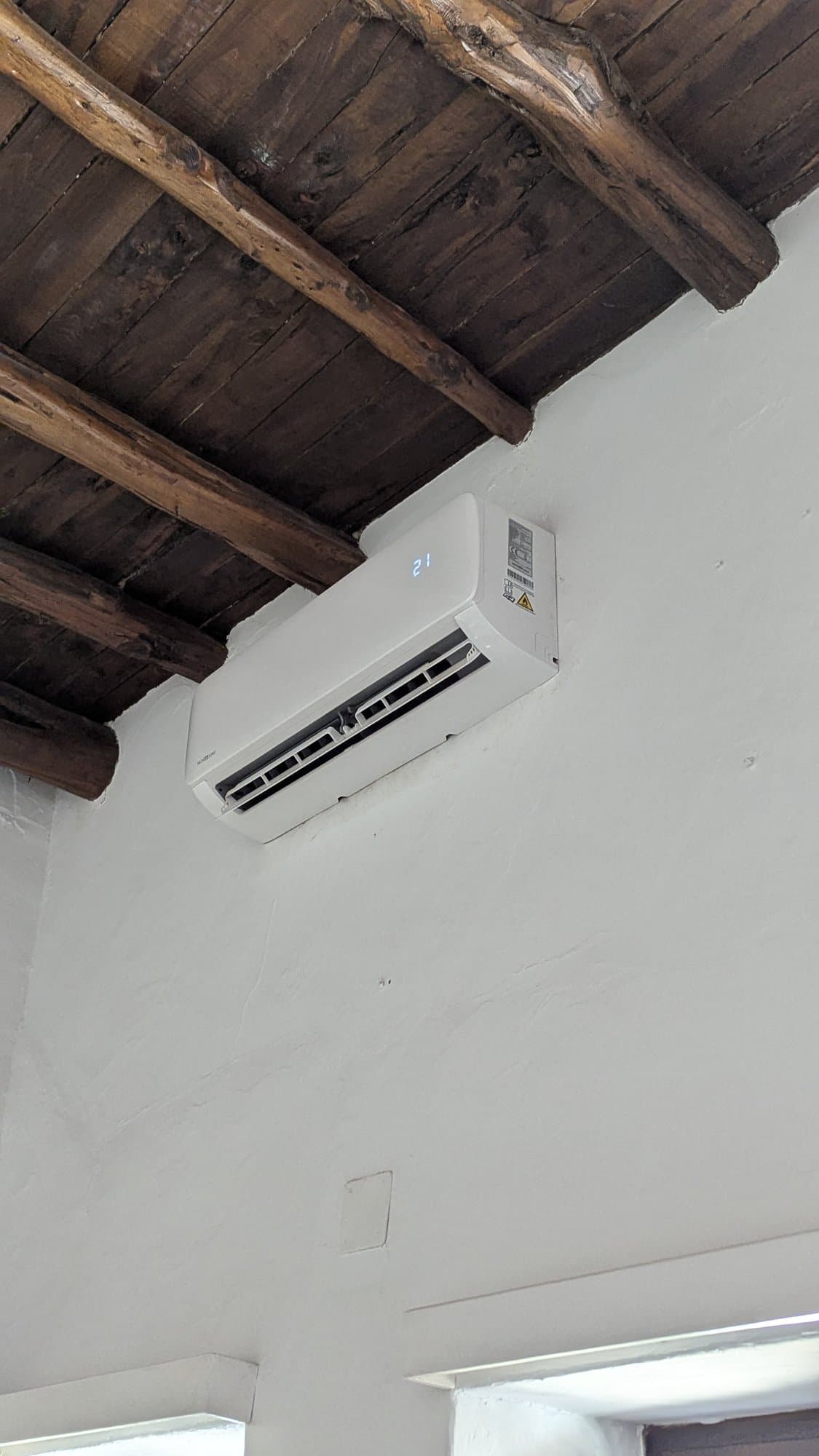 Wandunit van de airco onder een houten balkenplafond.