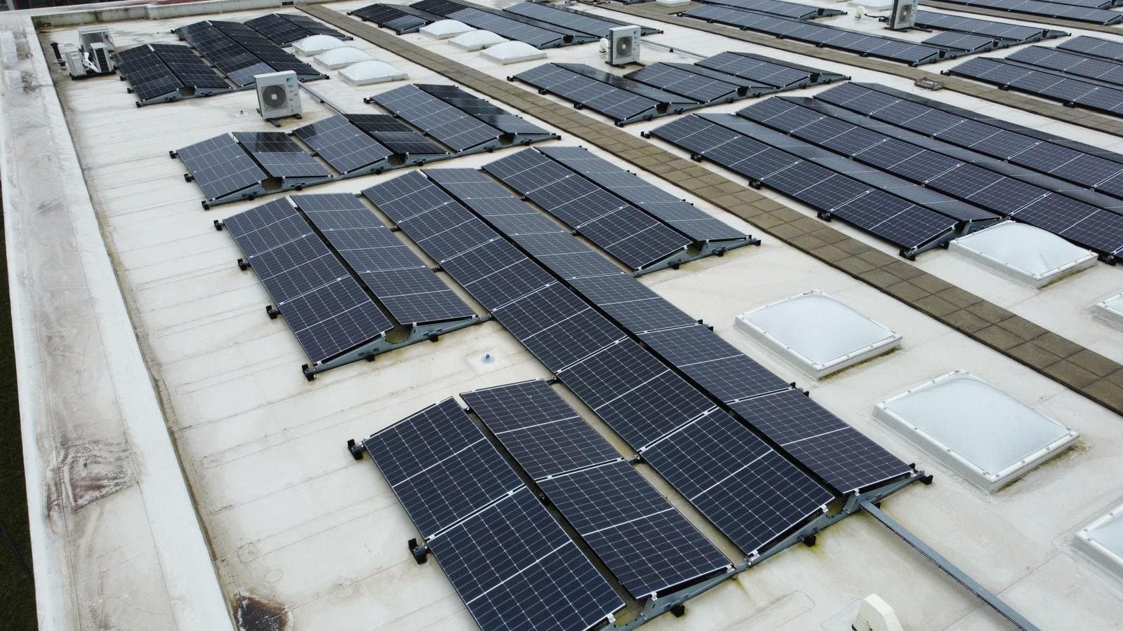 Overzicht van een plat dak met rijen zonnepanelen, lichtkoepels en buitenunits.
