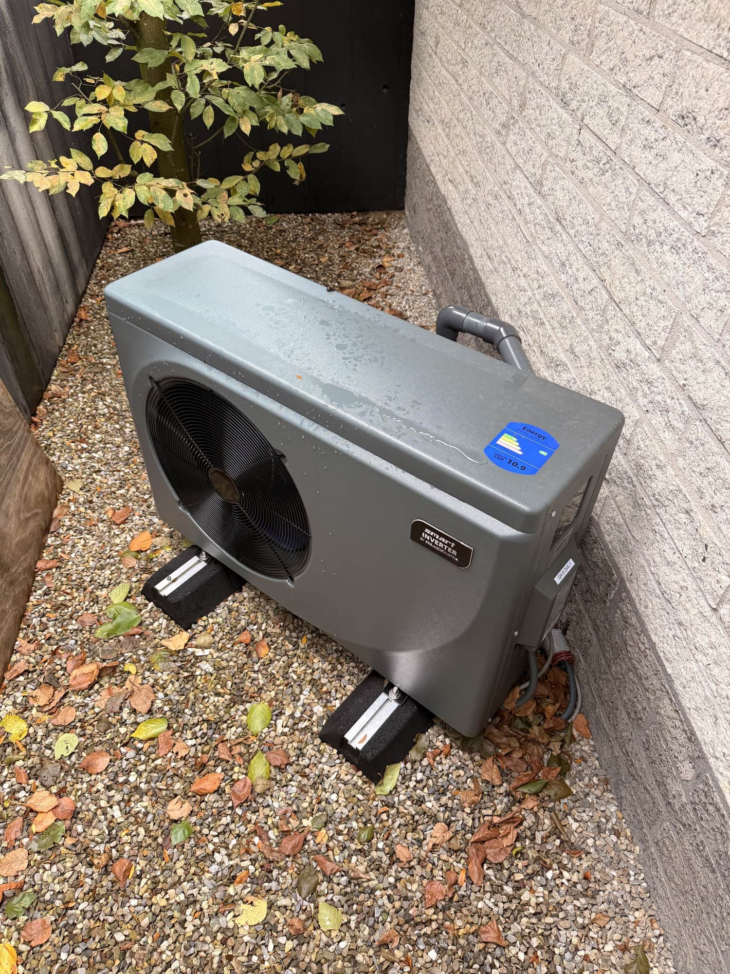 Buitenunit van de zwembadwarmtepomp op een grindstrook.